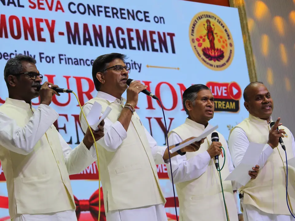 Two speakers at the podium beneath the banner for the National Seva Conference on Mind-Money Management