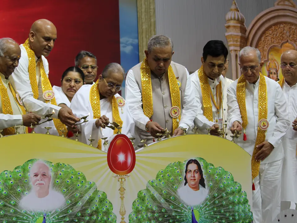 Dignitaries and Brahma Kumaris sisters lighting a ceremonial lamp on stage