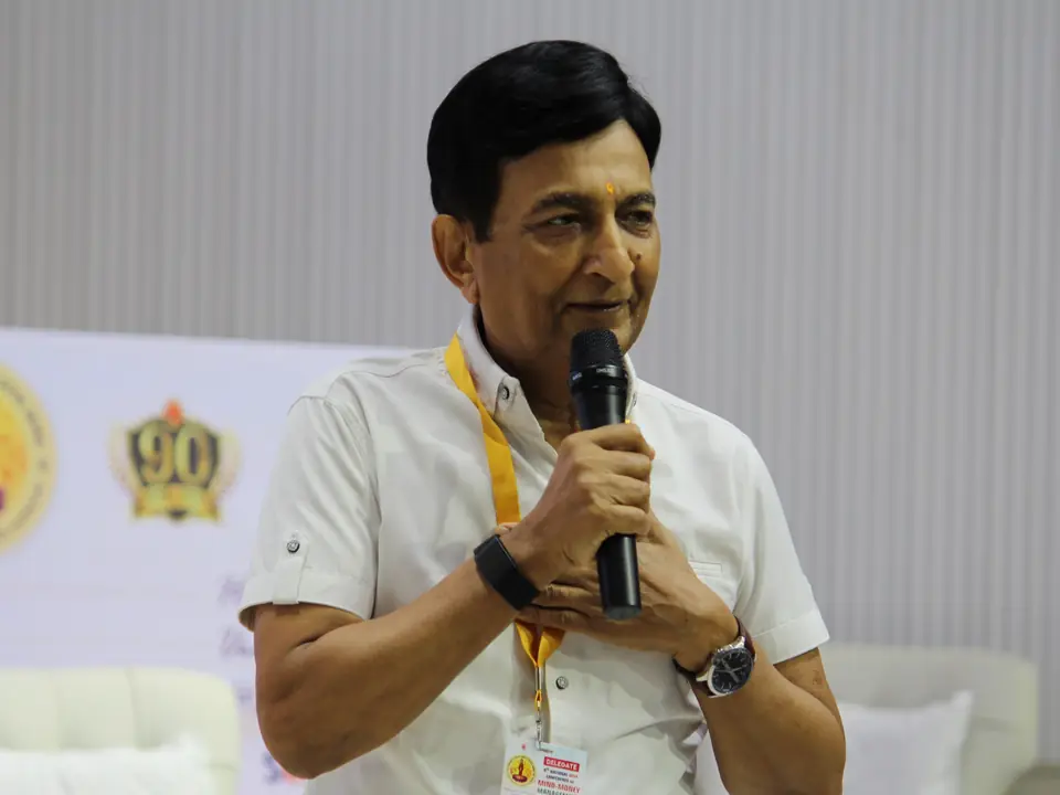 Dr. Jitendra Adhia addressing the hall with a handheld microphone